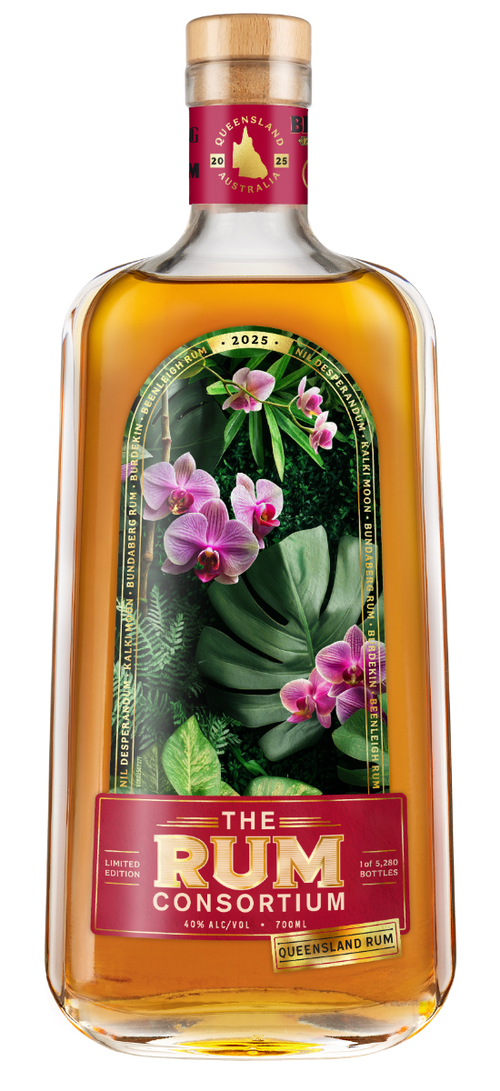 A clear glass rum bottle displays a botanical label with pink orchids and green leaves; amber liquid fills the bottle against a white background.