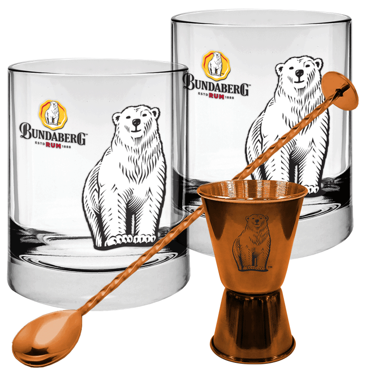Two clear glass tumblers printed with a standing polar bear and orange circular logo; a long copper spoon rests diagonally, its bowl balanced in a small copper jigger on a white background.