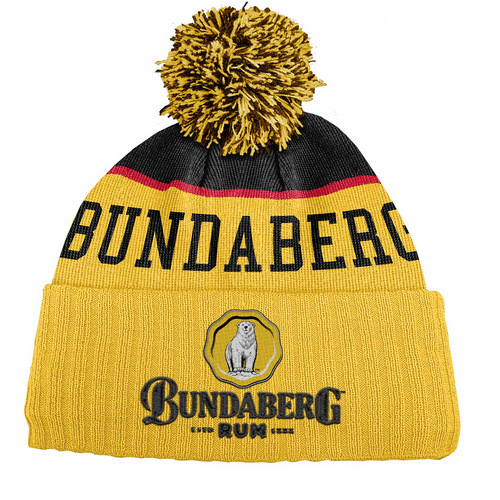 A yellow knit pom‑pom beanie with black and red stripe displays "BUNDABERG" across its band; lower cuff bears a circular logo reading "BUNDABERG RUM".