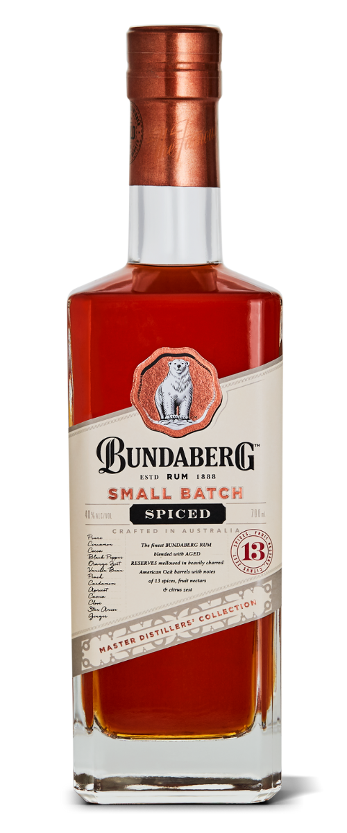A tall rectangular glass bottle of Bundaberg Small Batch Spiced rum stands upright, amber liquid visible; cream-and-red label with crest and copper-colored cap, isolated on a white background.